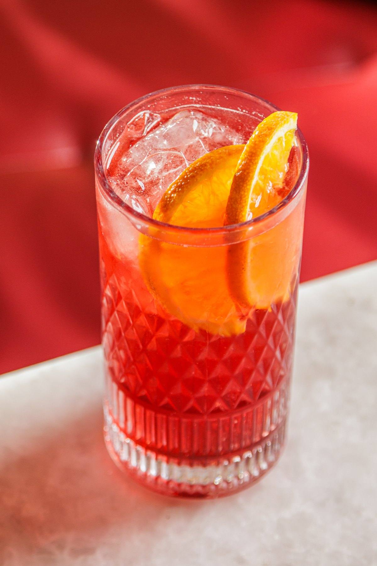 Campari tonic com gelo e rodela de laranja sobre mesa de mármore