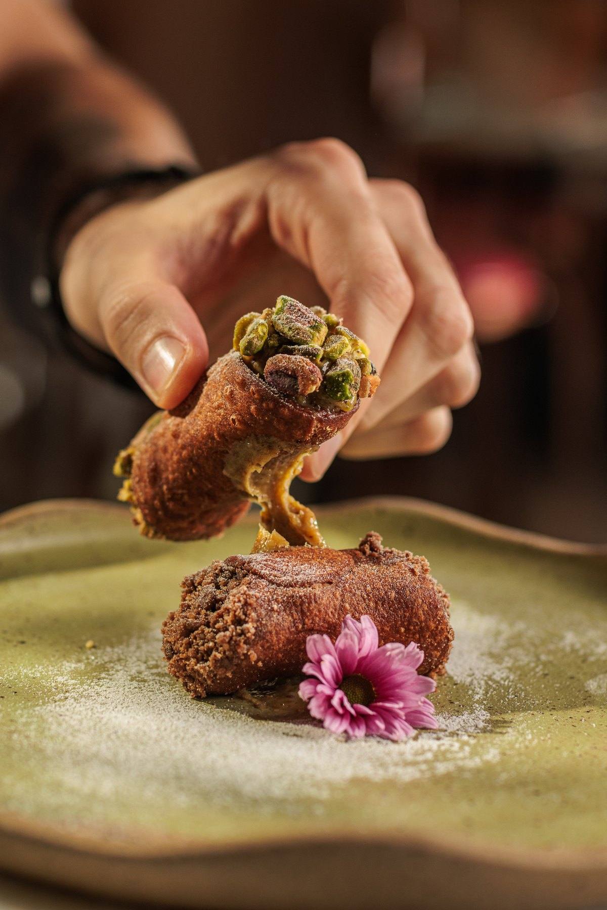 Mão segurando um cannolo siciliano com pistache
