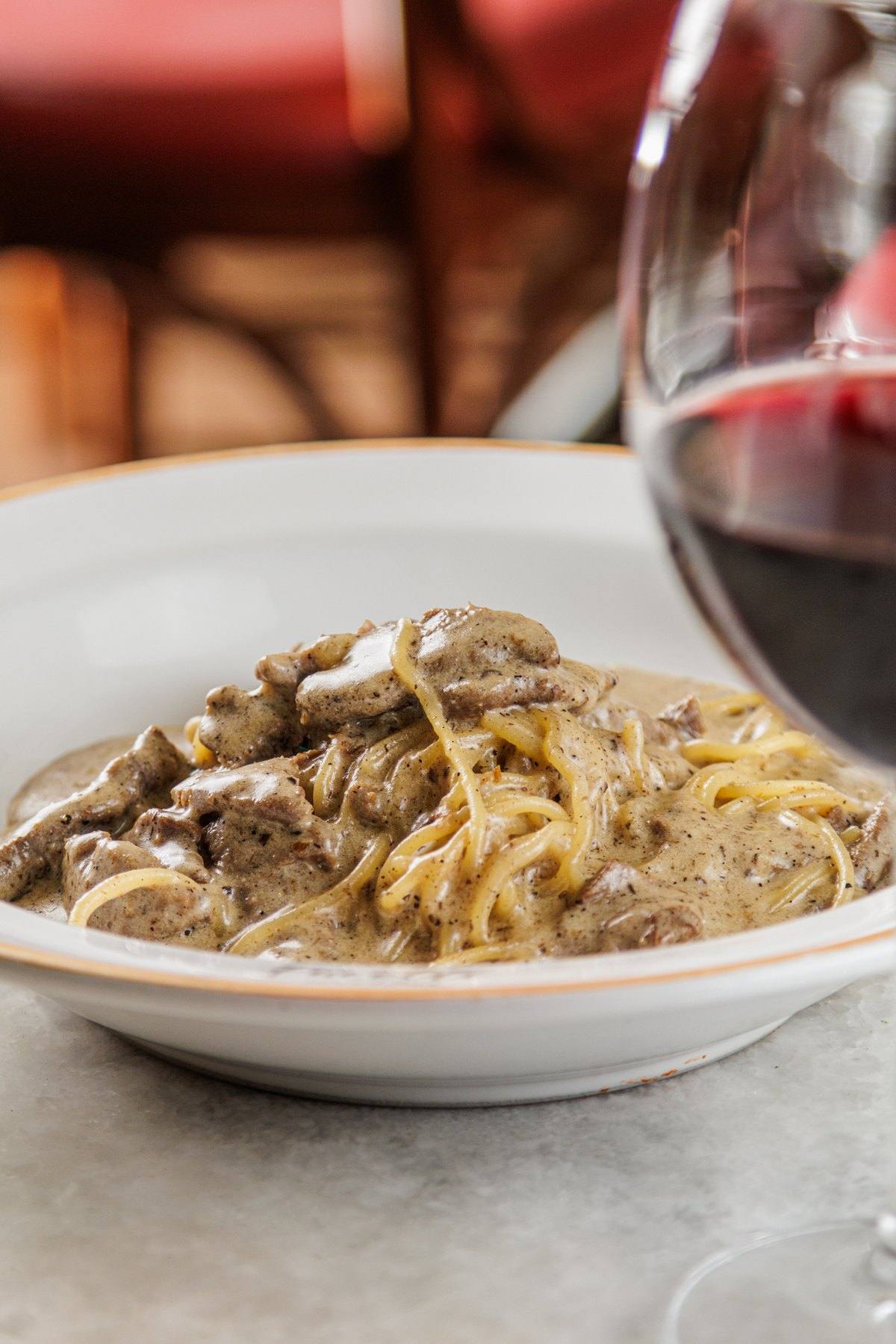 Spaghetti com iscas de filé mignon ao lado de uma taça de vinho tinto